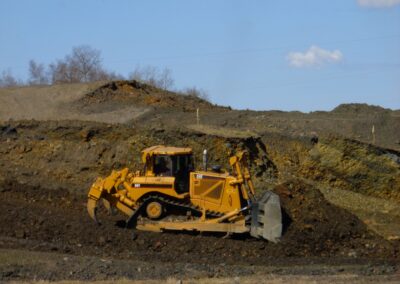 Bulldozer pushing rocky dirt and spoil material, surrounded by larger piles of waste rock