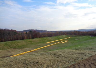Landscape view of large, grassy area sloping downward to flat basin area. Bright yellow baffles run the length of the basin.