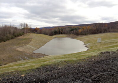 Newly construction detention basis filled with water; grass beginning to grow on slide slopes; woods in background