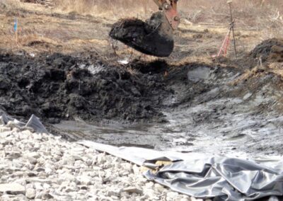 Excavator bucket scooping muddy dirt from new stream channel area