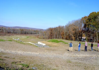 Five adults look towards landscape of a graded depression that will be a new stream channel.