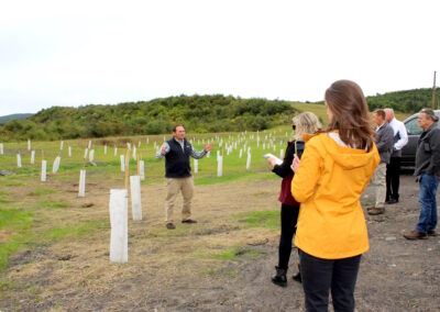 Terry Ostrowski talking on grassy area with newly planted saplings to attendees of press event.