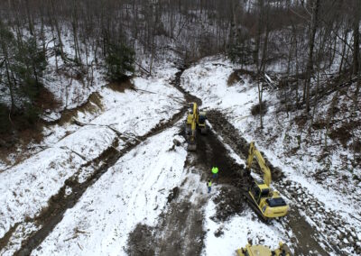 Aerial view of two excavators removing dirt from channel in wooded area.