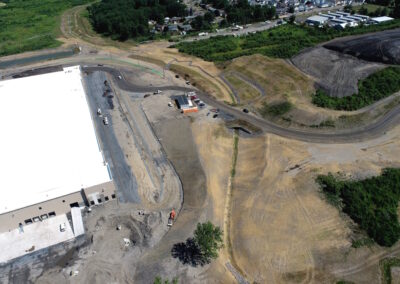 New stream channel on recently seeded land going under new bridge with warehouse on left-hand side.