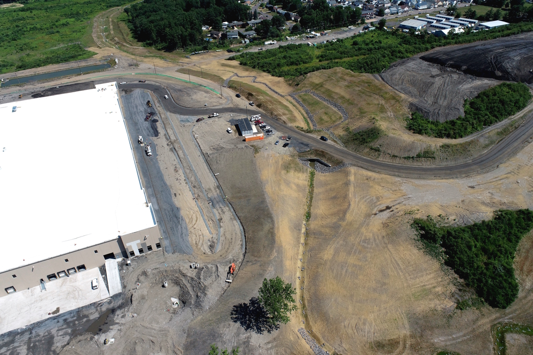 New stream channel on recently seeded land going under new bridge with warehouse on left-hand side.