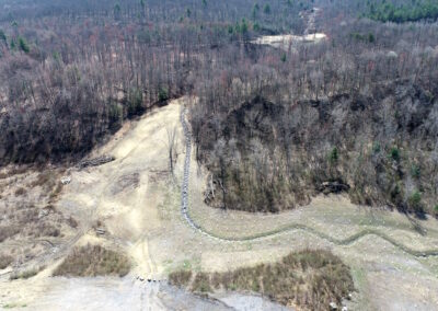 Aerial view of winding stream channel up cleared and newly seeded hillside with forest on both sides.