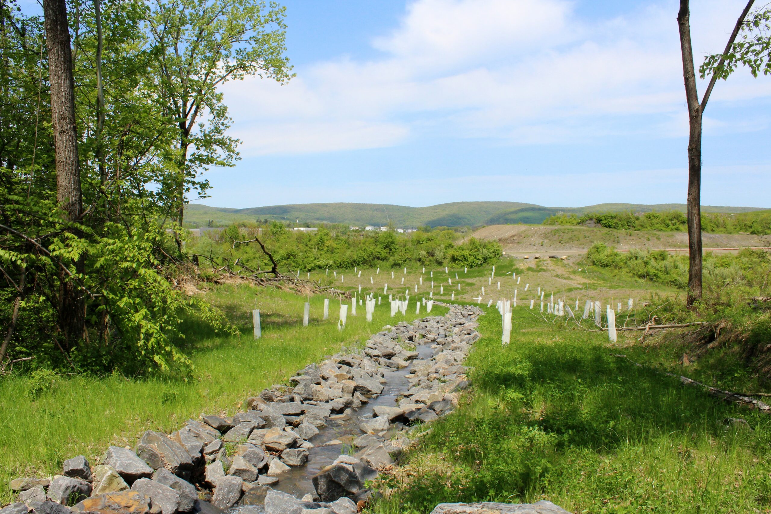 Constructed stream flowing down grassy hillside towards valley.