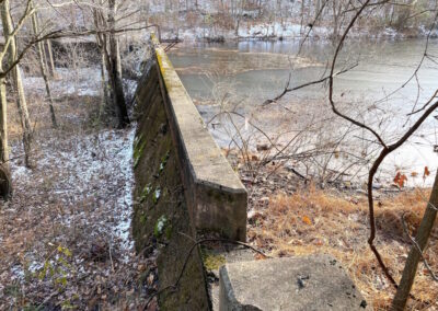 Old concrete dam structure in wooded area retaining silt pond on right-hand side.