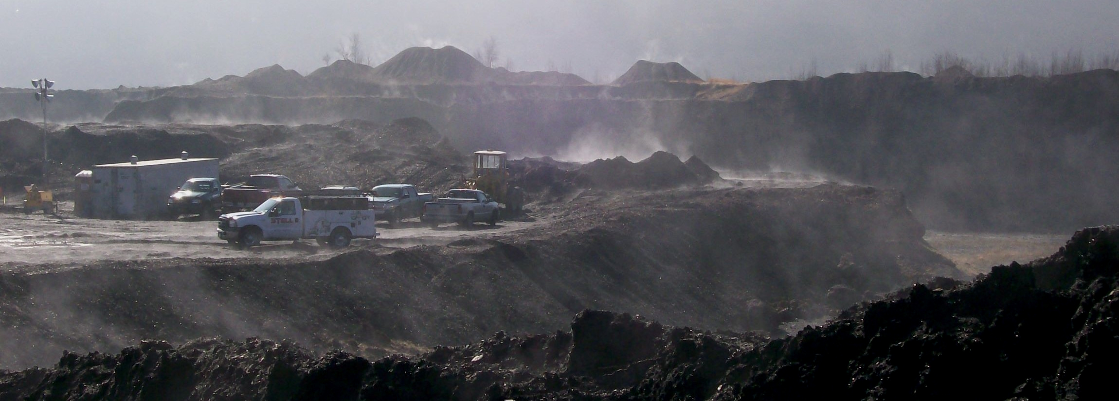 Bulldozer pushing spoil material amid large waste rock piles.