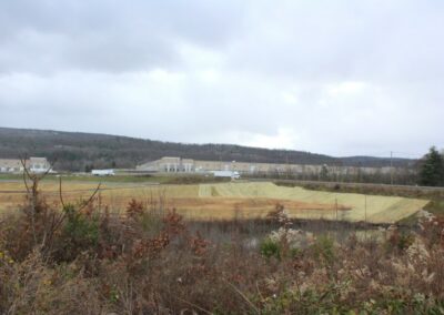 Flat area newly seeded, covered with straw mats. Two large warehouse buildings are in the background on a higher tier.