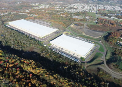 Drone image of two large warehouses with bare, flat area to the north.