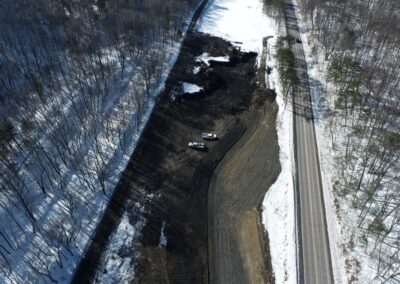 Aerial view of a construction site in a snowy forest area within the Nanticoke Creek watershed, showing earth-moving vehicles and a cleared dirt area with a trench being formed in the middle. Snow covers the surrounding ground and trees.