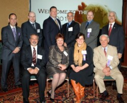 Adults in business wear pose for group shot; six are standing, four are seated