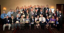 Large group of adults, some seated in front, many in business wear, pose for camera.