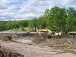 Several heavy construction vehicles (excavators) dig into dirt/muddy area.