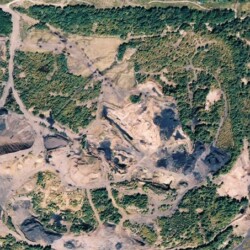 Satellite view of mine-scarred site with very unnatural, barren topography, large piles of mine spoils, surrounded by trees.