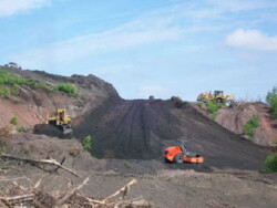 Heavy machinery works on creating a smooth, uphill slope in dirt-covered area for roadway