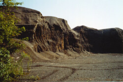Landscape view of what appear to be dirt mountains/cliffs. Brown material is piled mining waste/rock.