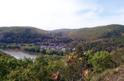 Landscape view from one small mountain ridge across valley with river to other small mountain with trees changing colors for fall. A small town is at the base of the mountain.