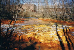 Grainy photo of orange stream flowing in front of several multi-story brick buildings
