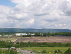 Landscape image from hill looking down on cleared, flat area. A semi-truck moves up a roadway in front of site to intersection.