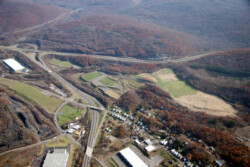 Aerial image of six reclaimed areas, covered in grass. Some have been turned into playing fields. Several roadways run alongside/in-between them. There is a residential neighborhood on right-hand side. Forested areas with autumn trees border area.