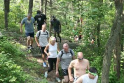 Line of adult runners heading downhill on hiking trail in woods.