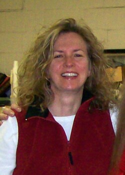 Torso/head picture of woman with blonde wavy hair in red vest and white shirt.