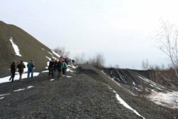 Line of 20+ adults walking up path on steep, unvegetated slope of coal waste