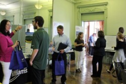 Adults standing in front of table displays speak with other adults about their companies.