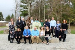 Approximately 20 adults standing around and sitting on statue of Penn State Nittany lion