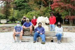 Group of adult students (wearing medical masks) sit around statue of Penn State Nittany lion